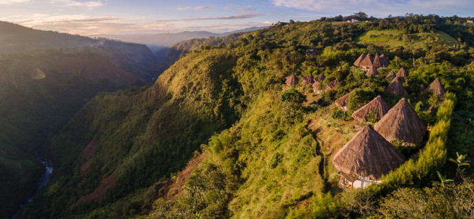 Panoramic view of traditional thatched-roof village in lush valley.