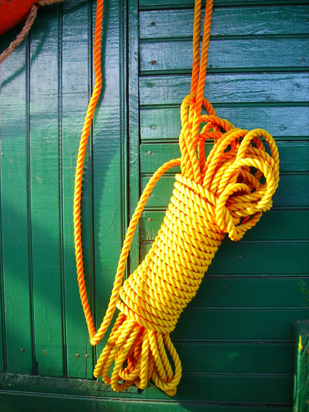 Corde enroulée jaune et orange sur fond de bois vert.