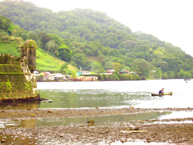 Côte tropicale avec ruines et pêcheur en bateau.
