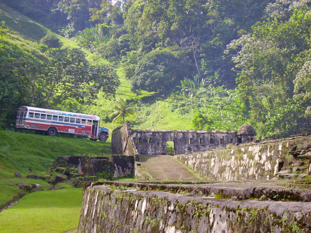 Bus passant par des ruines anciennes dans un paysage verdoyant.