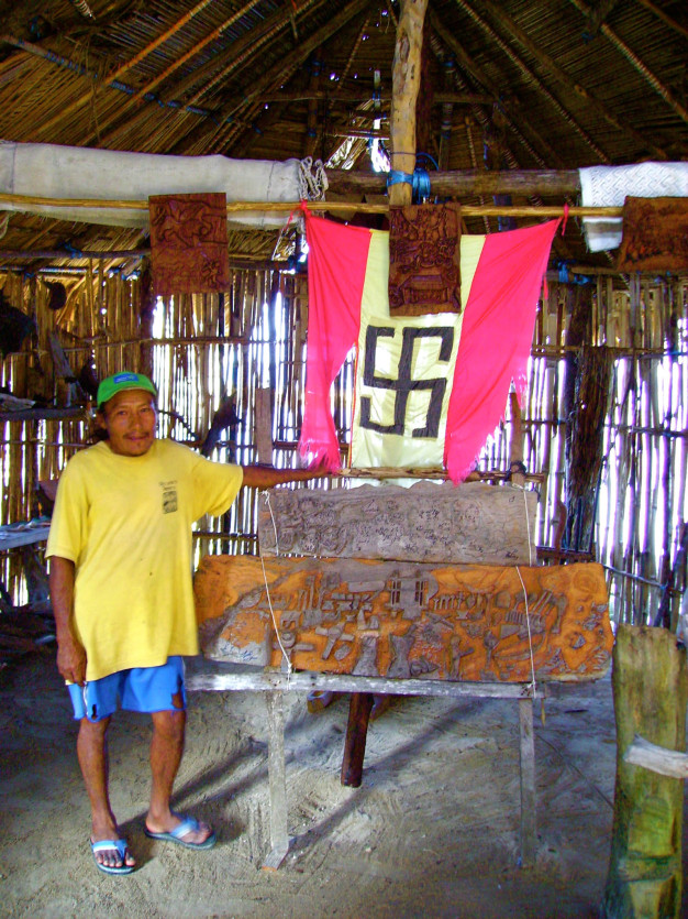 Homme à côté d'un banc sculpté dans une hutte traditionnelle.