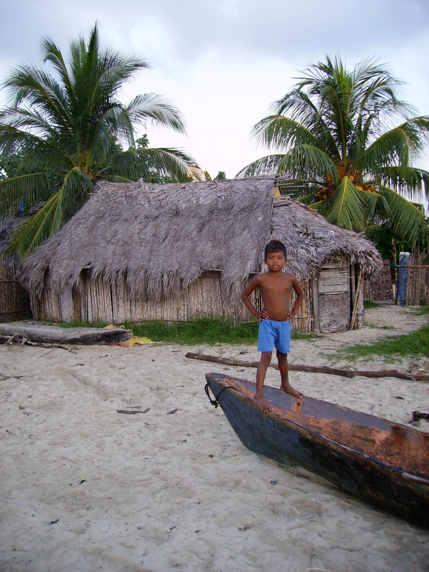 Garçon à côté d'un canoë sur fond de cabane de plage tropicale.