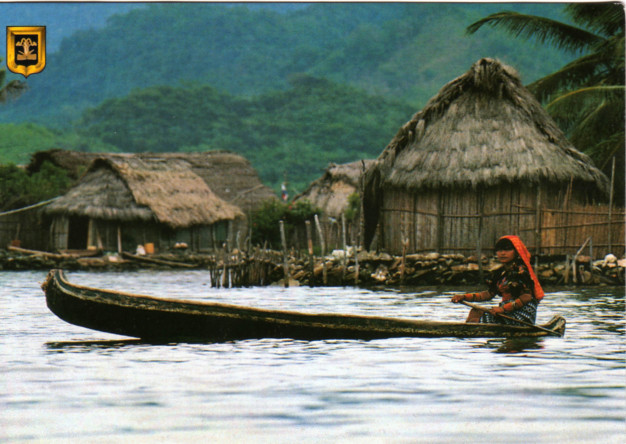 Personne pagayant en canoë près de huttes en chaume sur l'eau.