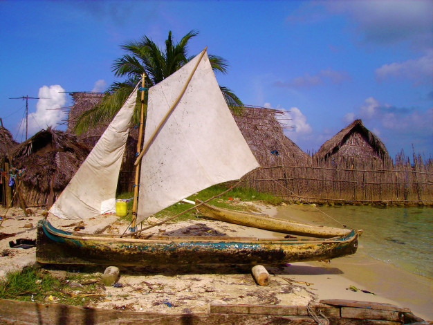 Voilier traditionnel sur une plage tropicale avec des huttes.