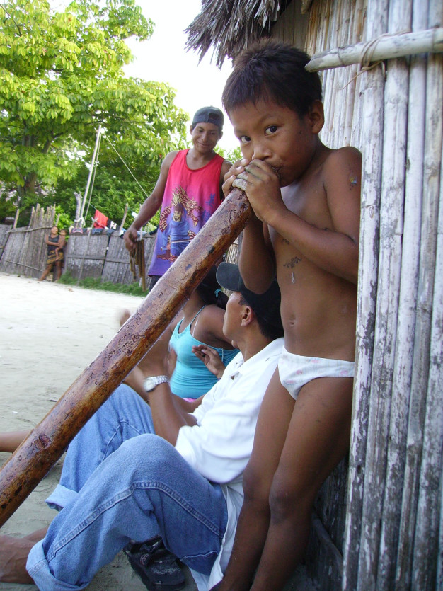 Enfant appuyé sur une poutre en bois avec une famille en arrière-plan.