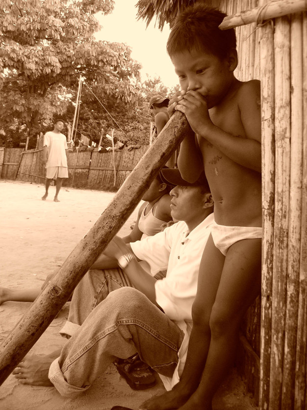 Enfant s'appuyant sur un poteau en bois avec des adultes en arrière-plan