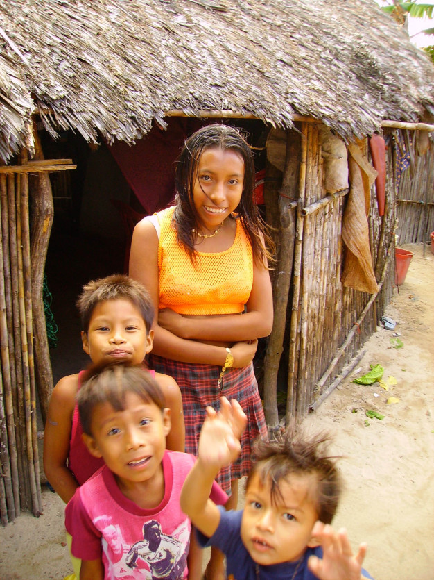 Enfants souriant à l'extérieur d'une hutte traditionnelle au toit de chaume.