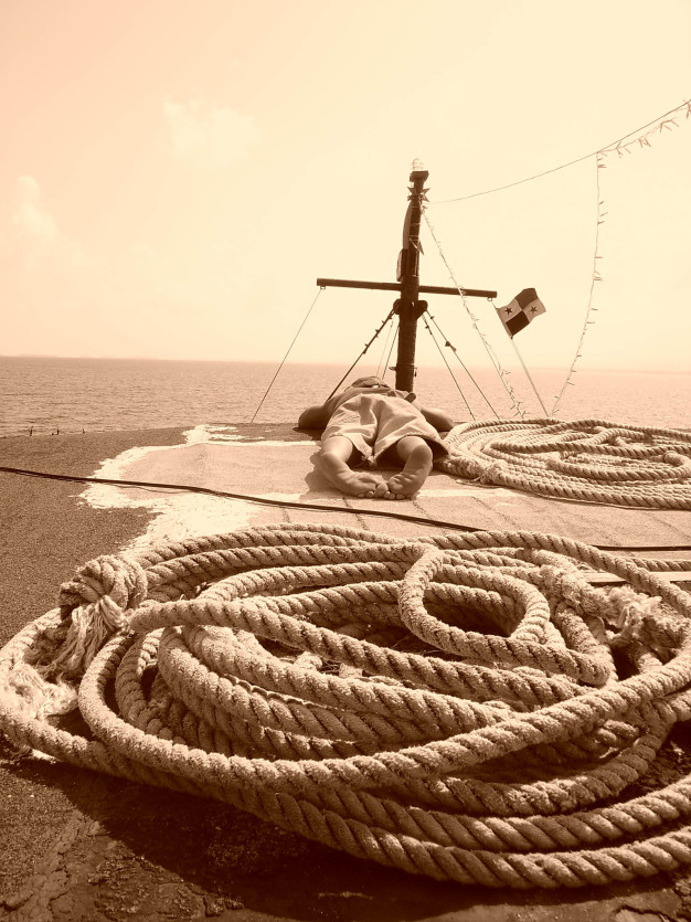 Mât de navire, cordages et vue sur l'océan en tons sépia.