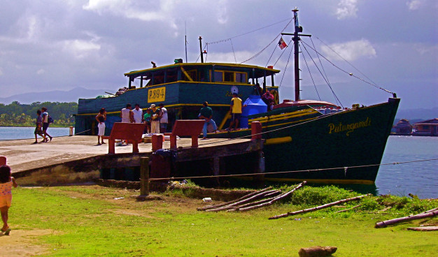 Passagers montant à bord d'un bateau coloré sur un quai tropical.