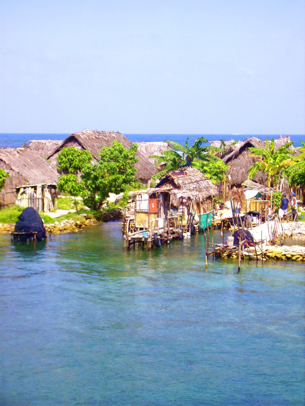 Village tropical en bord de mer, avec des cabanes au toit de chaume et des quais en bois.