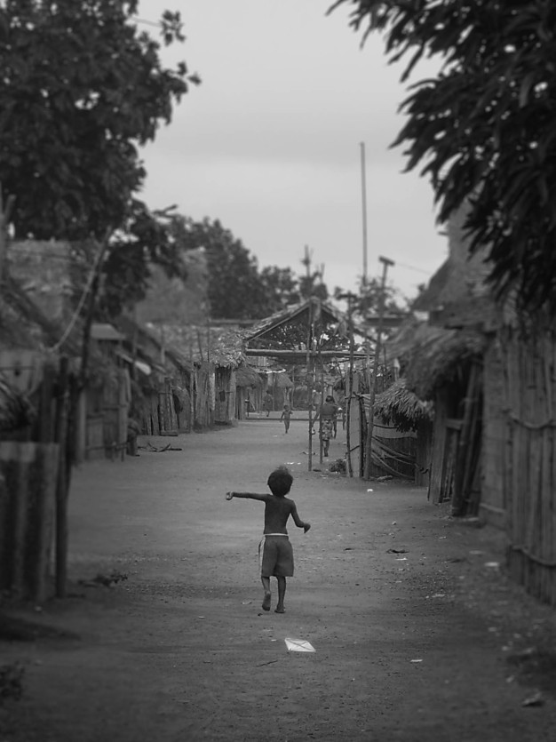 Enfant jouant dans la rue d'un village rural, noir et blanc.