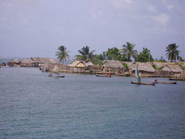Village tropical au bord de l'eau avec des huttes en chaume et des canoës.