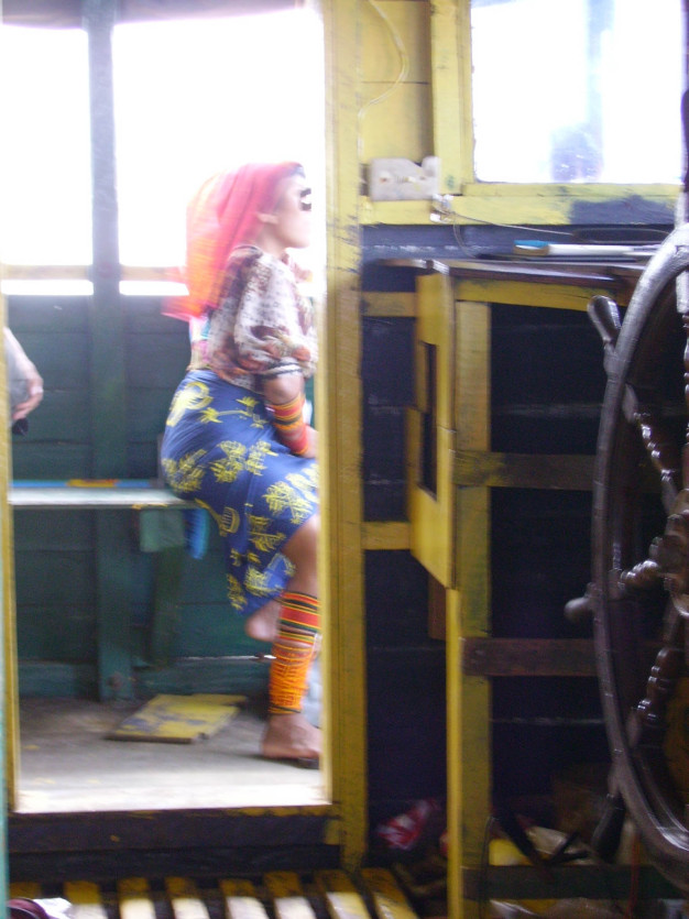 Femme en tenue colorée près de la barre à roue d'un bateau.