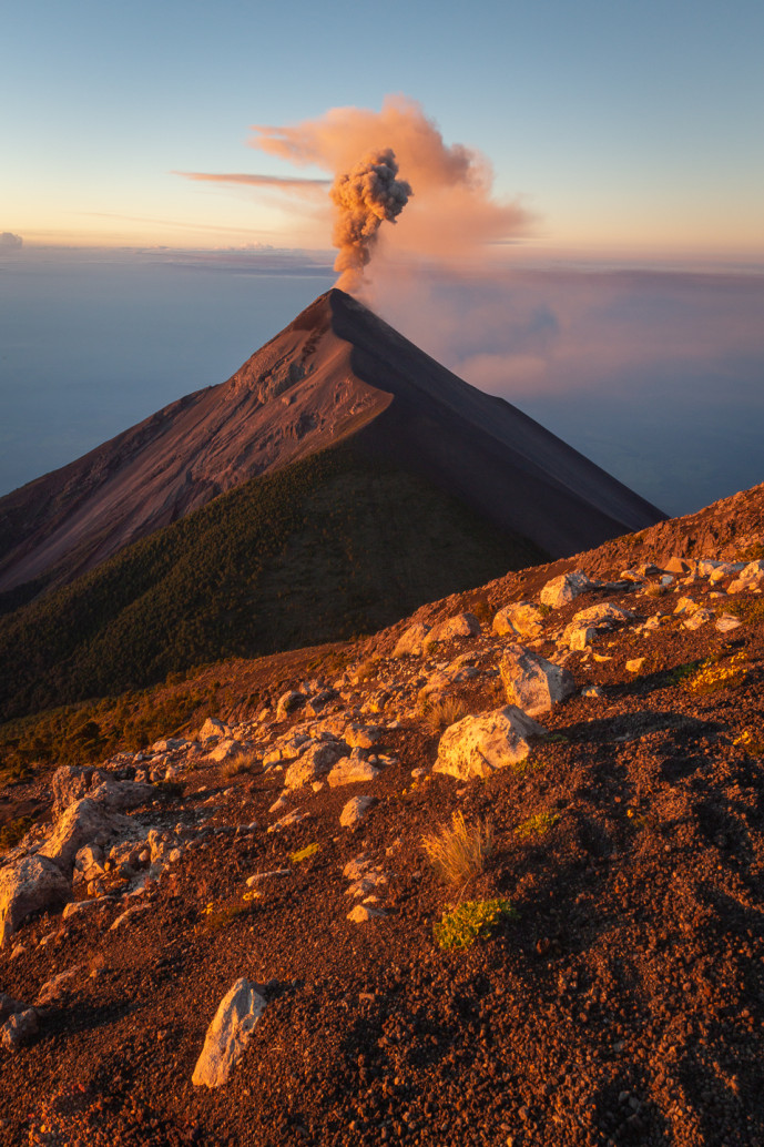 Volcan en éruption au coucher du soleil avec panache de cendres.