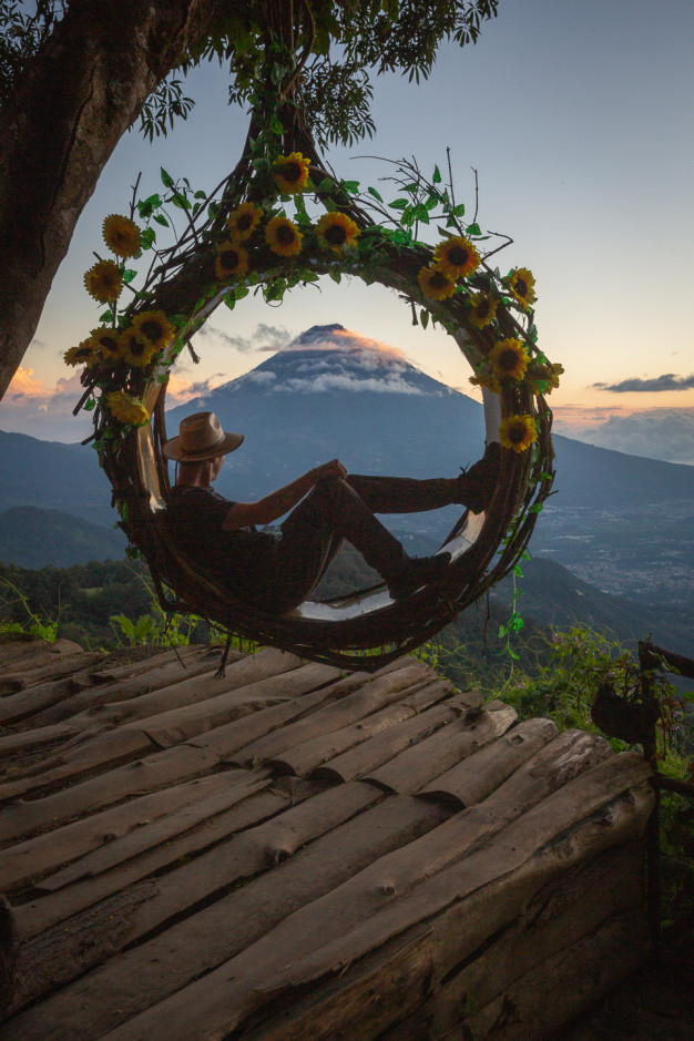 Person relaxing in sunflower swing with mountain view.
