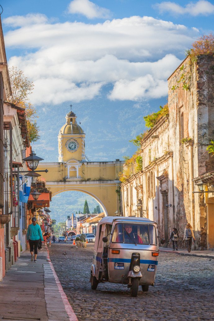 Rue coloniale avec arcade et tuk-tuk à Antigua, Guatemala.