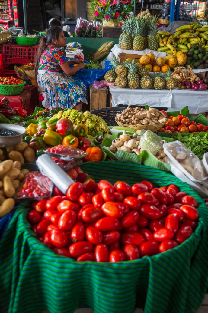 Femme à l'étal d'un marché de fruits et légumes colorés.