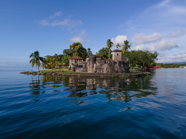 Historic stone fortress on tropical island with palm trees.
