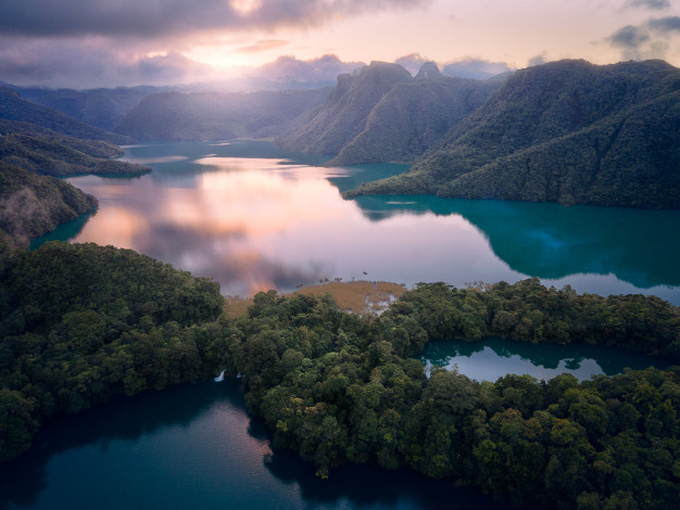 Scenic aerial view of a tranquil, forested lake at sunrise.