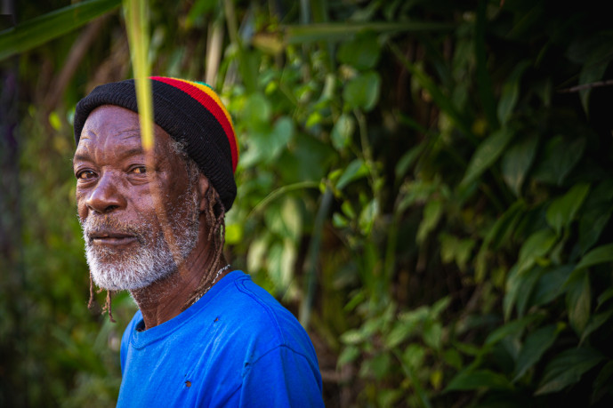 Homme en rastaquouère en plein air près d'un feuillage vert.