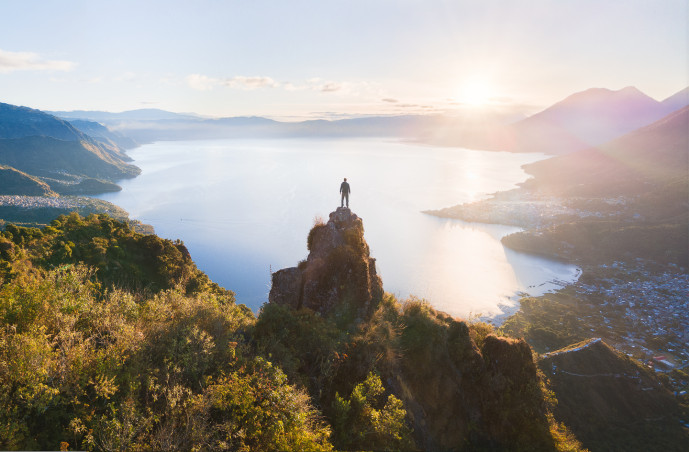 Personne au sommet d'une montagne surplombant le lever du soleil et le lac