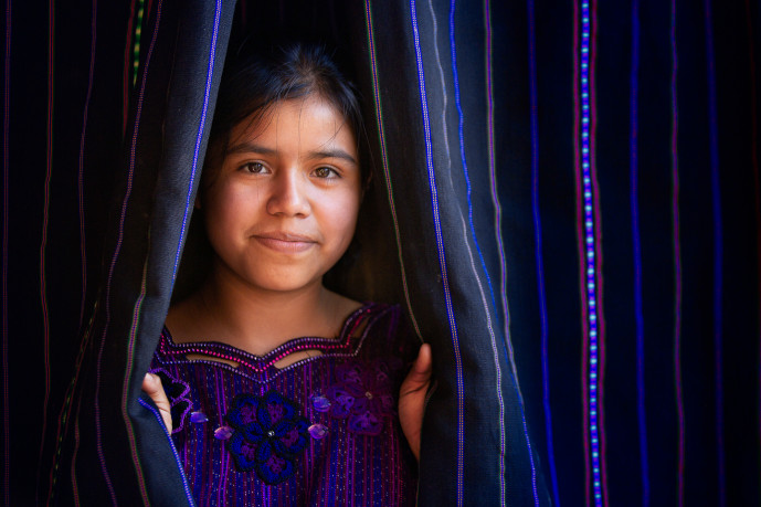 Fille souriant entre des textiles rayés colorés.