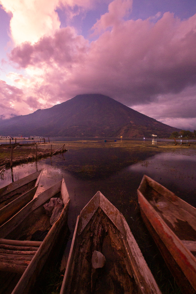 Sunset over mountain with wooden canoes on lake.
