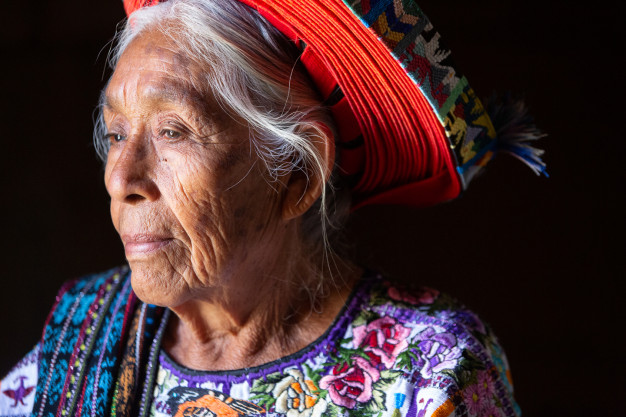Elderly woman in traditional embroidered dress and headwrap.