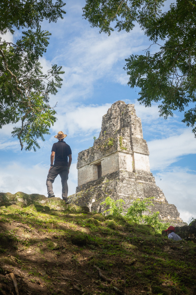 Man overlooking ancient Mayan temple ruins in jungle.