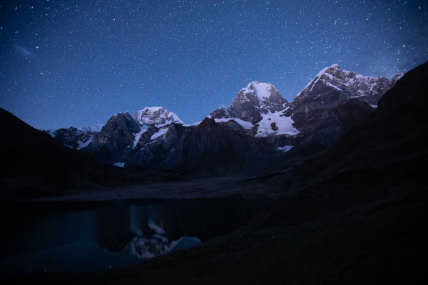 Starry night over mountainous terrain with reflective lake.