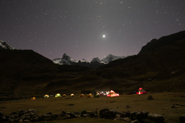 Illuminated tents under starry sky in mountainous terrain.