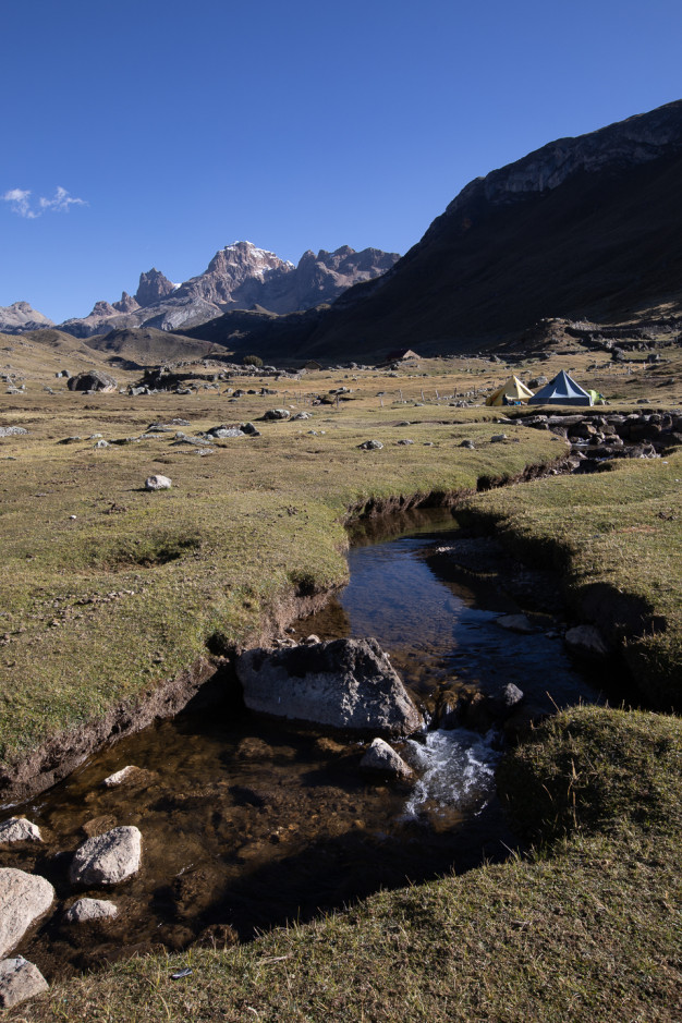 Mountain campsite with tents and stream.