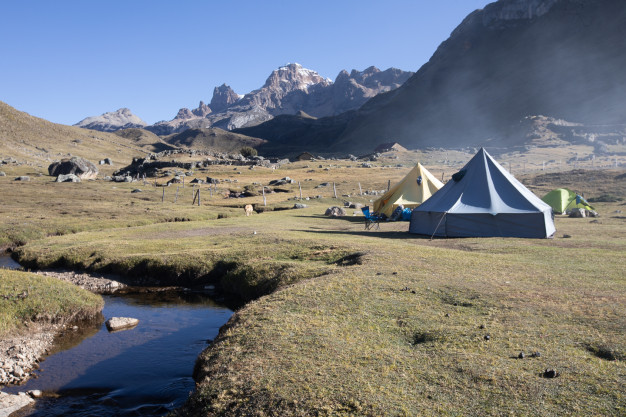 Camping de montagne avec tentes près d'un ruisseau.