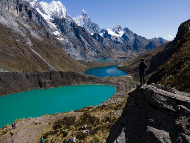 Randonneur surplombant des lacs glaciaires turquoise dans un paysage montagneux.
