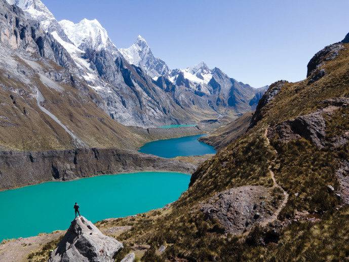 Hiker overlooking turquoise lakes and snowy mountains.