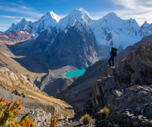 Hiker overlooking turquoise lake and snowy mountain peaks.