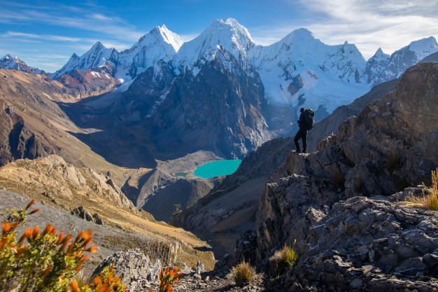 Hiker overlooking turquoise lake and snowy mountain peaks.