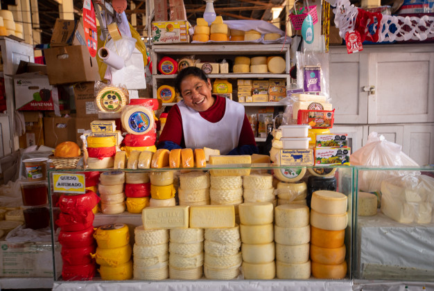Vendeur de fromage souriant derrière son étal de marché avec divers fromages.