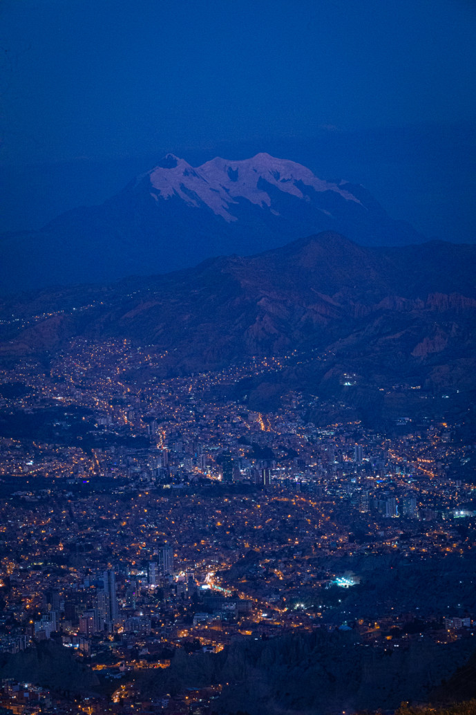 Nighttime cityscape with snow-capped mountain backdrop.