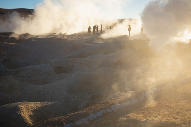 Visitors at geothermal springs with steam at sunrise.