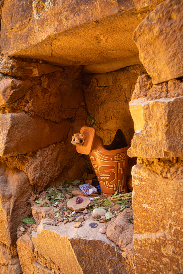 Pot en céramique et offrandes dans une niche rocheuse.