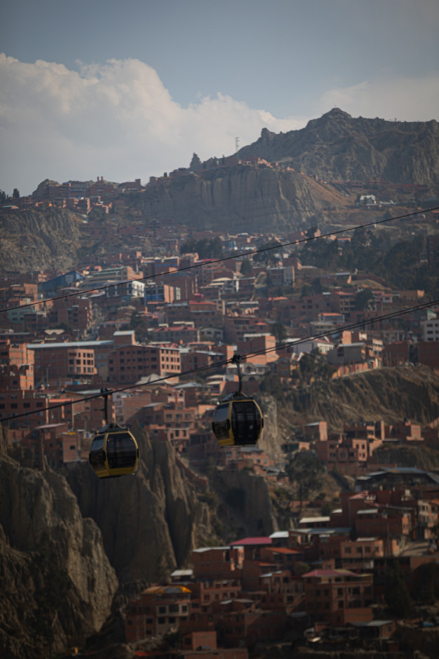 Cable cars over hilly cityscape with rocky backdrop.