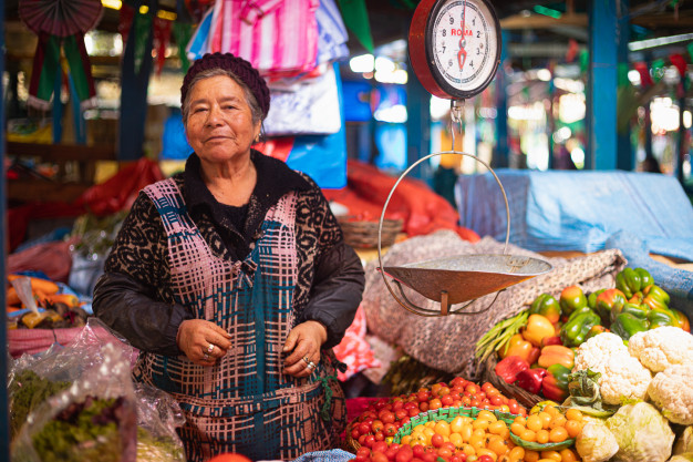 Femme vendeuse à l'étal d'un marché de légumes colorés.