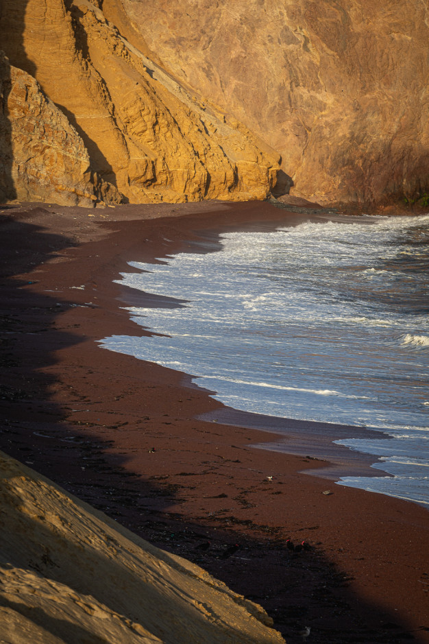 Cliffside with red sandy beach and waves