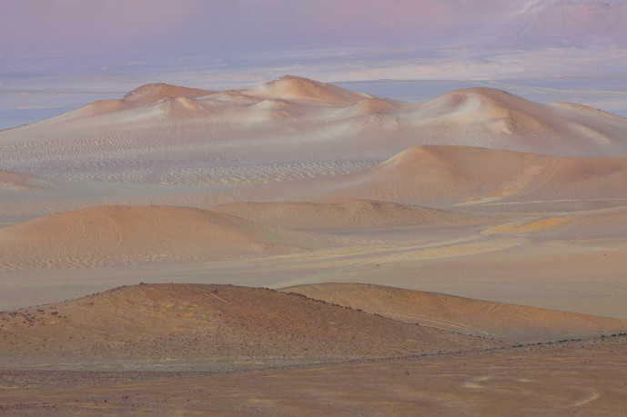 Desert landscape with colorful hills and textured sand.