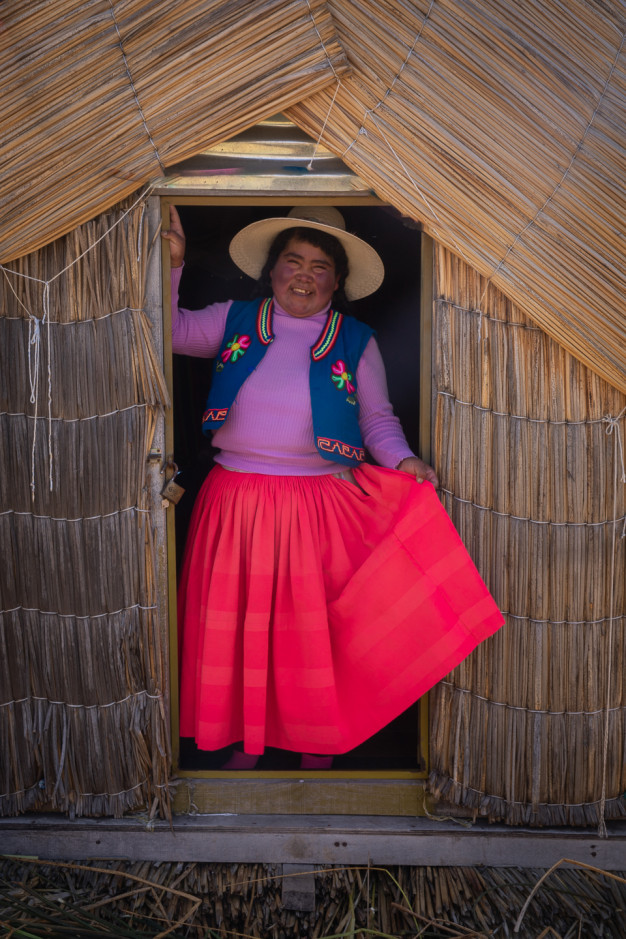 Femme en tenue traditionnelle à la porte d'une hutte de roseaux.