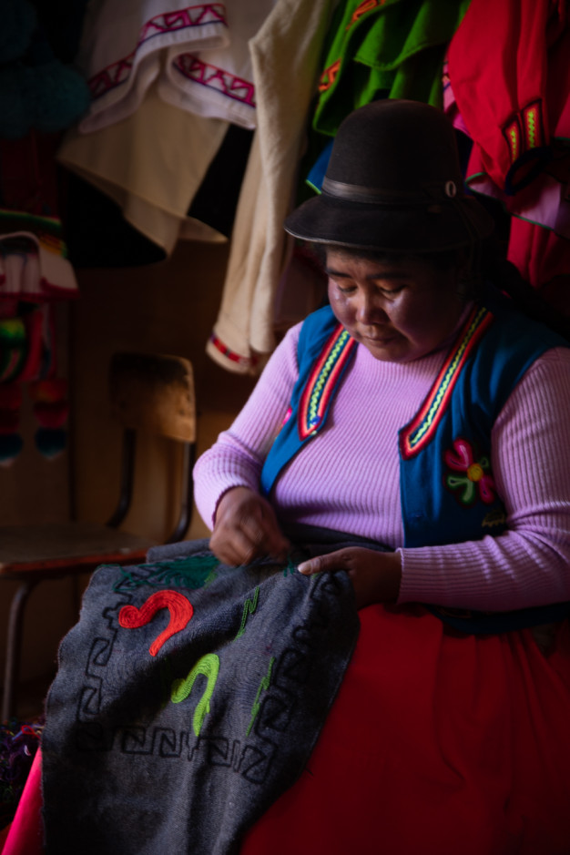 Femme brodant un textile traditionnel dans une tenue colorée.