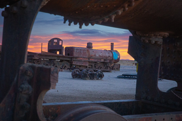 Vestiges de trains rouillés au coucher du soleil dans un paysage désertique.