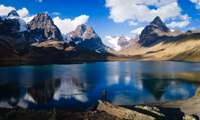 Person by mountain lake with snowy peaks.