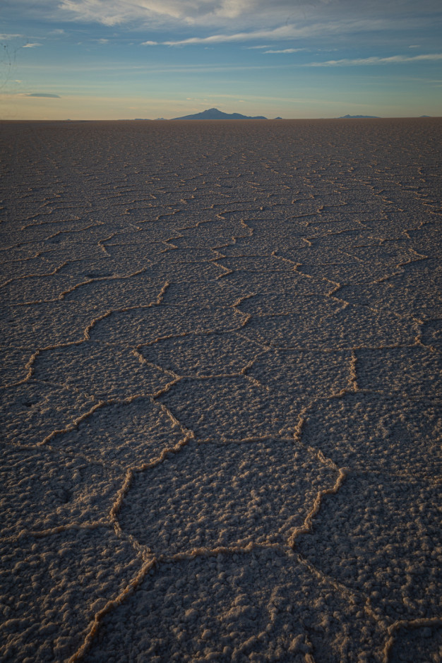 Sunset over cracked salt flats, mountains in distance.